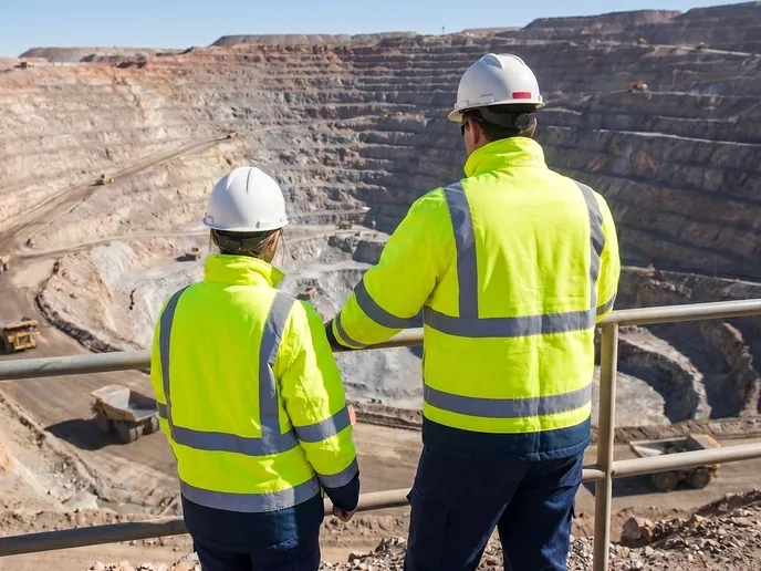 Two mine engineers in high-visibility gear looking out over the benches of an open pit